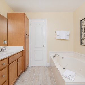 Refreshing master bath featuring a jetted tub, walk-in shower, modern cabinetry, and elegant wall decor