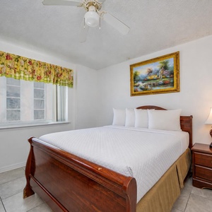 The master bedroom features a queen bed with floral bedding, a TV, and a lovely view from the large window