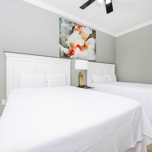 This guest bedroom features two comfortable queen beds, a stylish lamp, and a colorful abstract painting above