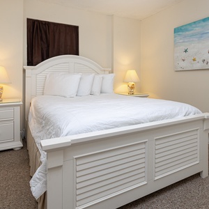 This cozy guest bedroom features a white bed with plush pillows, soft lighting, and beach-themed decor for a relaxing stay