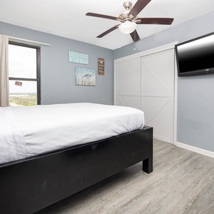 This cozy bedroom features a comfortable queen bed, a mounted TV, and beach-themed decor, perfect for a relaxing getaway