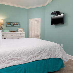 This bedroom features a calming teal wall, a cozy king quilted bed, and a wall-mounted TV for your entertainment
