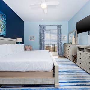 Brightly colored artwork complements the serene blue walls in this inviting master suite with a king bed and beach balcony