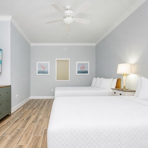 Inviting guest room featuring two queen beds, a large TV, and cheerful coastal artwork for a restful stay