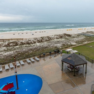 The view showcases a tranquil beach with white sand, lounge chairs, and a gazebo in the pool area, inviting relaxation