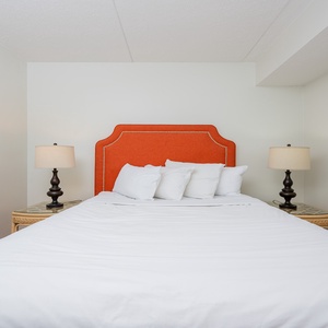 The bedroom features a vibrant orange headboard, soft bedding, and bedside lamps for a relaxing stay