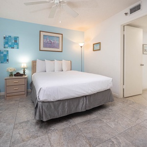 Brightly decorated guest bedroom featuring a queen bed, bedside lamp, and artwork, with a window allowing natural light