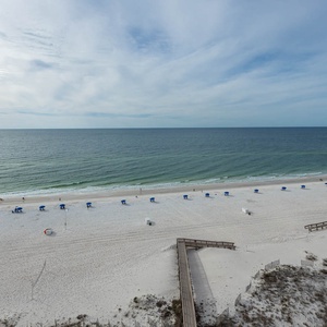 Enjoy the view of the serene beach lined with blue umbrellas and gentle waves under a serene sky