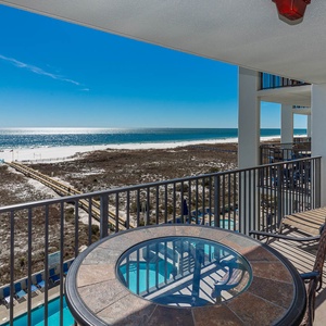 Balcony with a round table and chairs overlooks the beach, showcasing the sparkling gulf and white sand shoreline