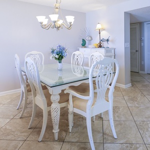 Bright dining area features a glass-top table surrounded by elegant white chairs, complemented by a charming chandelier