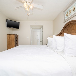 This cozy bedroom features a wooden headboard, a mounted TV, and a serene atmosphere perfect for relaxation