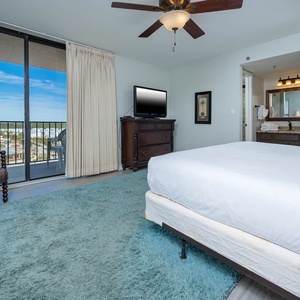 The master bedroom features a plush rug, king bed, a TV for entertainment, and a lovely view from the balcony