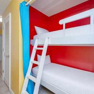 This colorful sleeping nook features a white bunk bed against a vibrant red wall, creating a fun space for kids or guests