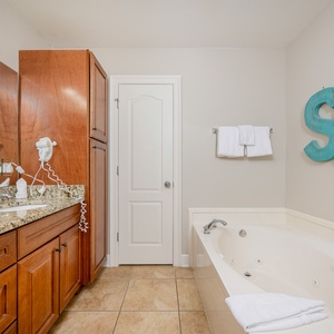 Refreshing master bath featuring a jetted tub, walk-in shower, elegant granite countertops, and coastal decor