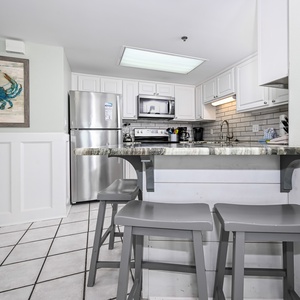 Bright kitchen area featuring a stylish marbled countertop, sleek appliances, and a cozy breakfast bar with gray stools