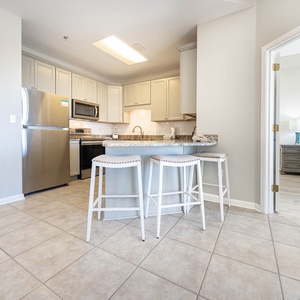 Kitchen area features a breakfast bar with white stools, granite countertops, and stainless appliances