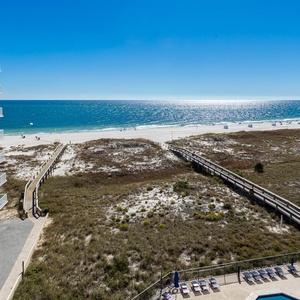 Views of the beach stretch beyond the wooden boardwalk, leading to the sparkling gulf waters under a clear blue sky