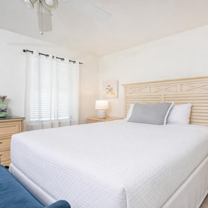 Bright and airy guest bedroom featuring a queen bed, decorative accents, and soft natural light from sheer curtains
