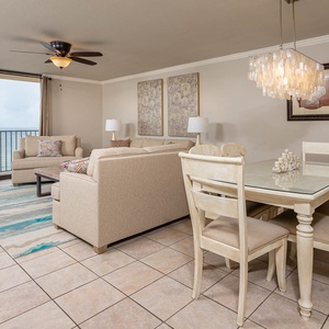 Inviting living area features a cozy sofa with queen sleeper, stylish dining table, and balcony with a beautiful beach view