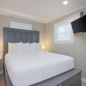 The master bedroom features a plush bed with white linens, a mounted TV, and soft lighting for a relaxing retreat