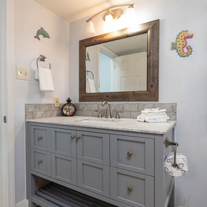 The bathroom features a stylish gray vanity with a marbled countertop, a large mirror, and neatly arranged towels