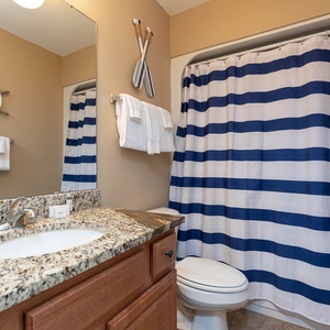 This bathroom features a granite countertop, navy and striped shower curtain, and nautical decor for a refreshing retreat