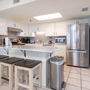 Bright kitchen featuring white cabinetry, a marbled countertop, and a breakfast bar with wooden stools for casual dining