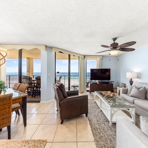 Bright living area features a comfortable sofa, dining space, and expansive views of the beach through large windows