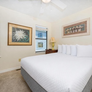 This cozy bedroom features a comfortable bed, lovely artwork, and a view of lush palm trees outside the windows