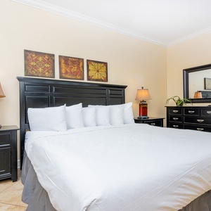 This bedroom features a king bed, elegant black furniture, colorful artwork, and soft white bedding for a restful retreat