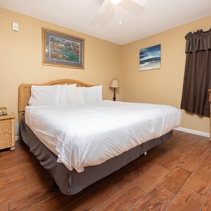 Cozy bedroom featuring a king bed, wicker furniture, and a flat-screen TV, complemented by warm, inviting decor