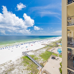 Vibrant beachfront view with white sand, colorful umbrellas, and the pool area visible from the balcony