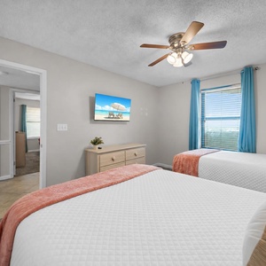 This guest bedroom features two double beds with colorful throws, a TV mounted on the wall, and natural light