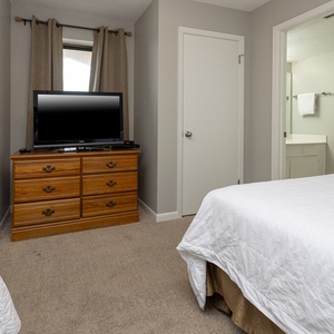 The guest bedroom features double beds, a wooden dresser with a TV, and an adjoining bathroom visible through a door