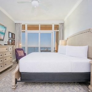 Relax in the inviting master bedroom featuring a king bed, a stylish chair, and beautiful beachfront views