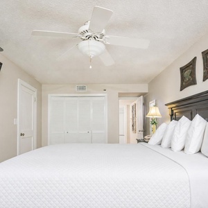 The master bedroom features a large king bed with fluffy white pillows, a mounted TV, and tasteful beach-themed decor