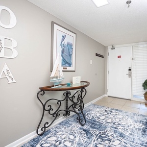 A welcoming entryway features a decorative console table, nautical artwork, and a vibrant area rug against tiled flooring