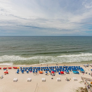 This balcony view showcases vibrant blue and red beach umbrellas lining the shore, inviting relaxation by the water