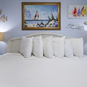The bedroom features a cozy white bed adorned with plush pillows, beach-themed artwork, and soft lighting for a relaxing stay