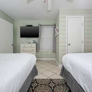 Guest bedroom featuring two queen beds, a mounted TV, and light green walls, creating a relaxing atmosphere for visitors