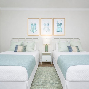 Cheerful guest bedroom featuring two comfortable queen beds and playful swimwear art for a fun getaway
