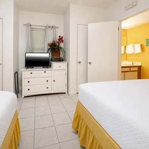 Relax in this bright guest room featuring queen beds, a TV, and a cheerful view into the adjoining bathroom area
