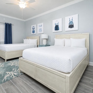 Relax in this guest bedroom with two queen beds, stylish decor, and fun swimsuit artwork on the walls