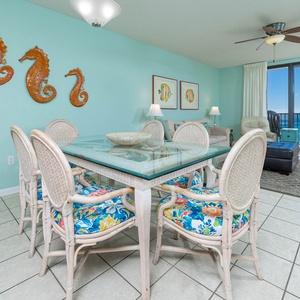 Gather around the glass dining table with colorful seating, enjoying the beach views through the balcony doors