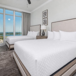 Unwind in a queen bed beneath a bedside lamp while floor-to-ceiling windows frame the gulf and shoreline