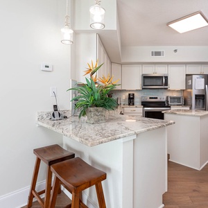 This modern kitchen features sleek stainless appliances, granite countertops, and a cozy breakfast bar with two wooden stools
