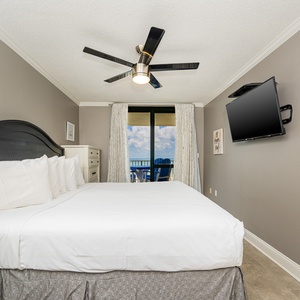 Stylish master bedroom featuring a king bed, a mounted TV, and access to a balcony with a view of the gulf