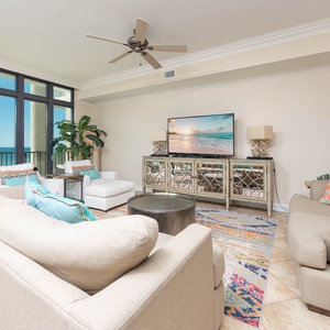 Living area featuring plush seating, queen sofa-sleeper, a large TV, and panoramic views of the sparkling coastline
