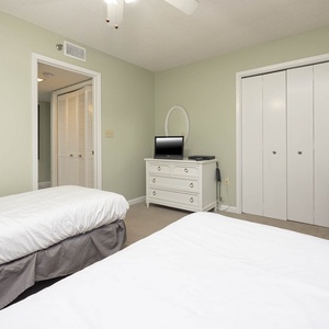 Bright guest bedroom featuring two twin beds, a dresser, a TV, and a charming floral arrangement on a nightstand