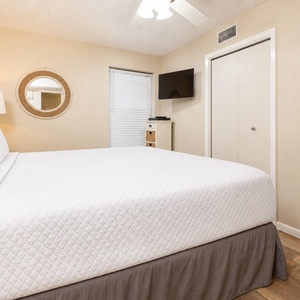 A cozy bedroom features a king bed, a wall-mounted TV, and a round mirror, creating a welcoming atmosphere